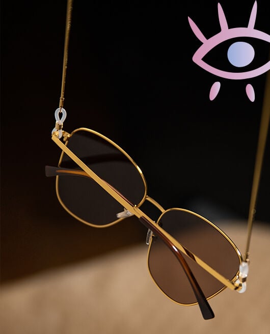 Eine Sonnenbrille mit goldenem Metallrahmen h&auml;ngt an einer D&uuml;nnen braunen Brillenkette
